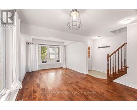 A spacious room with wooden floors and a staircase.