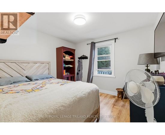 A bedroom with a bed, a fan, and a window with a view of trees.