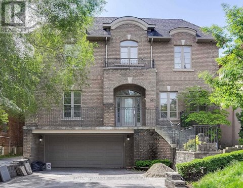A large, two-story house with a garage is surrounded by greenery.