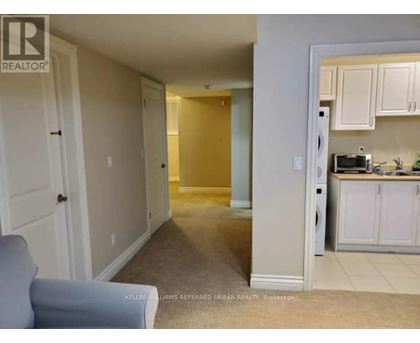 A living room with a grey couch and a kitchen area in the background.