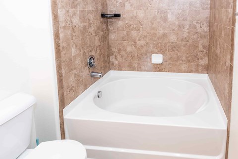 A white bathtub is in a bathroom with brown tiles.
