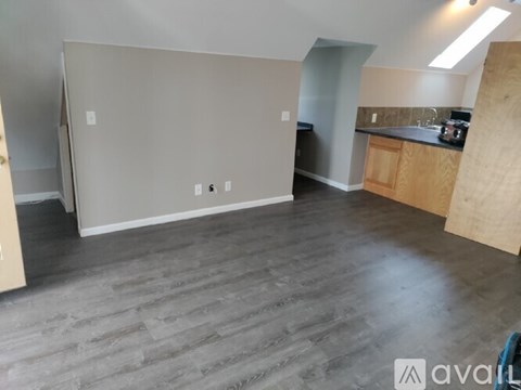 A room with a grey floor and a kitchen area in the background.