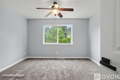A room with a ceiling fan and a window showing trees outside.