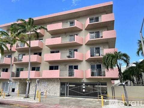 A pink and white building with balconies and palm trees in front.