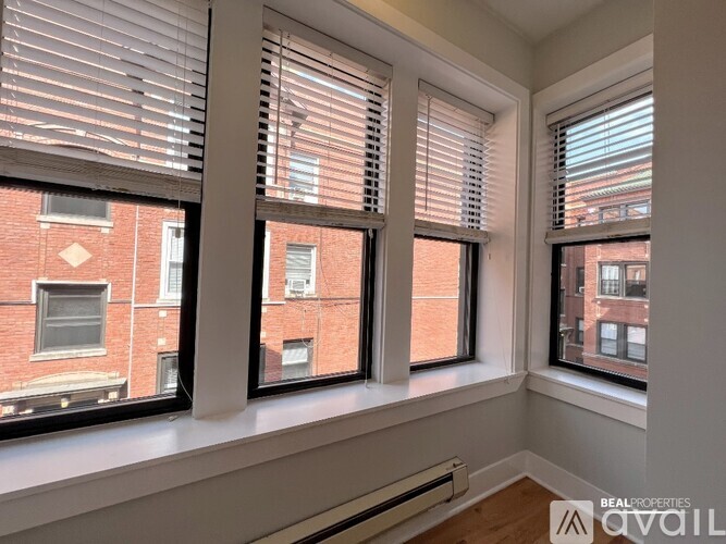 A room with three windows showing a view of a brick building outside.