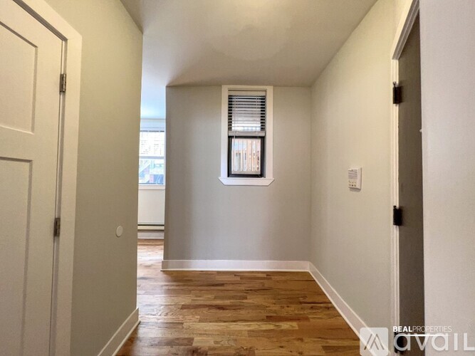 A hallway with wooden floors and white walls leading to a window.