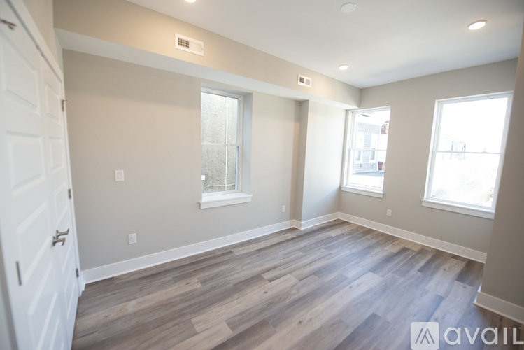 A spacious room with wooden flooring and two windows.