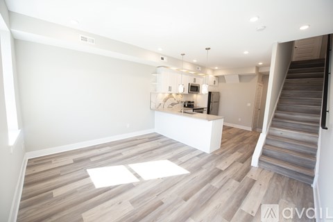 A spacious room with wooden flooring and a kitchen area in the background.