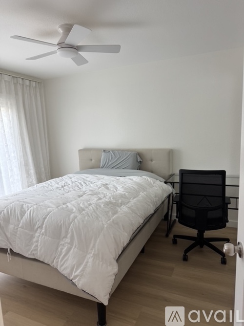 A bedroom with a white bed and a black office chair.