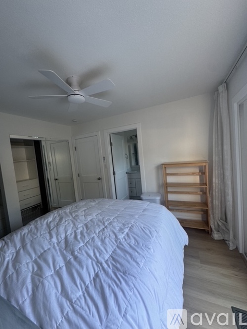 A bedroom with a white bedspread and a ceiling fan.