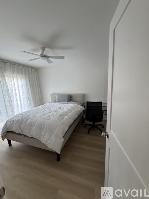 A bedroom with a bed, chair, and ceiling fan.