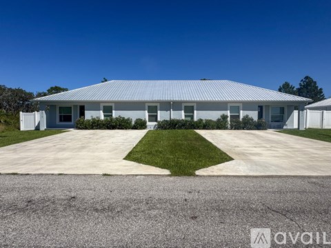 A white building with a corrugated metal roof and a gravel driveway in front.