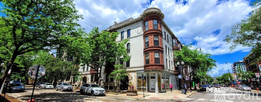 A street view of a multi-story building with a red awning and a tree in front of it.