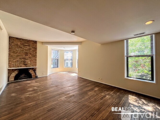 A spacious room with wooden flooring and a brick fireplace.