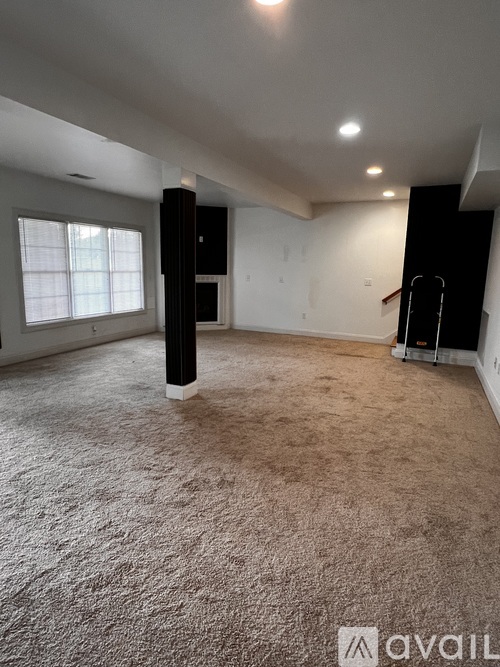 A spacious room with a carpeted floor and a window on the left side.