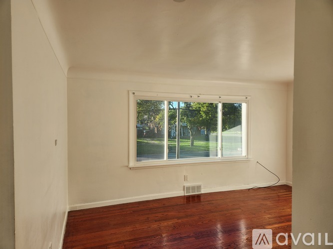 A room with a large window and wooden flooring is available for rent.