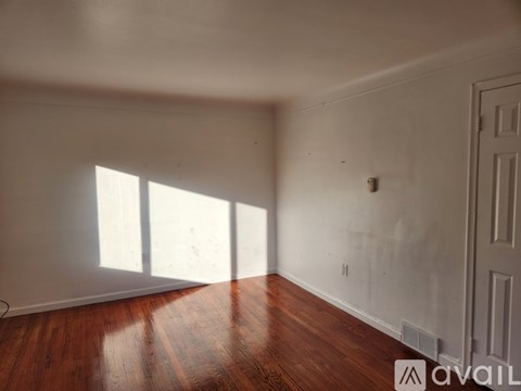 A room with wooden floors and white walls, with a door on the right side.