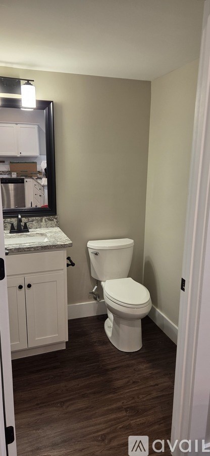 A white toilet in a bathroom with a wooden floor and a mirror above the sink.