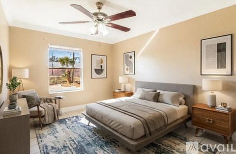 A bedroom with a large bed, a ceiling fan, and a view of a balcony through the window.
