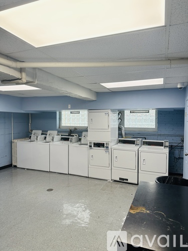 A room with a row of washing machines and a trash can.