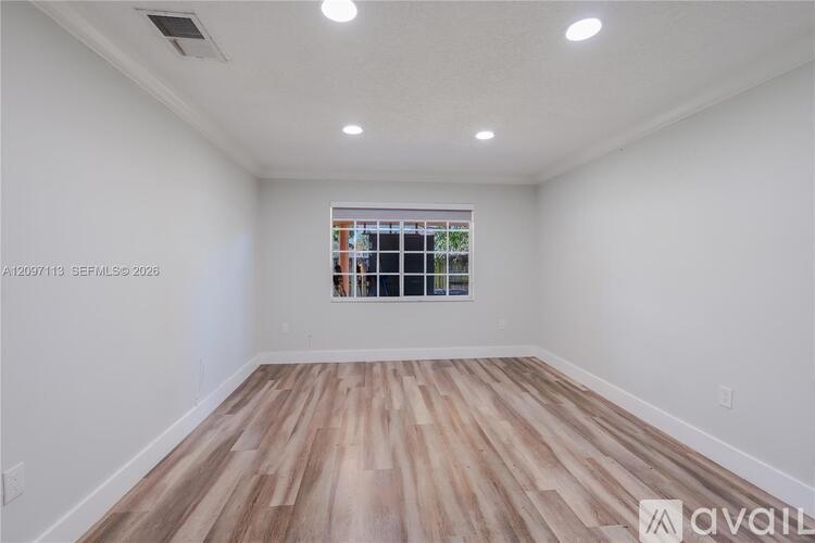 A room with wooden flooring and a window showing a view of a building.