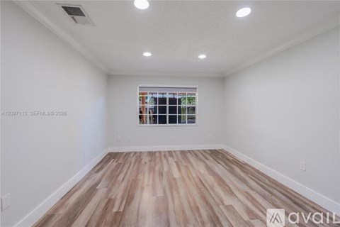 A room with wooden flooring and a window showing a view of a building.