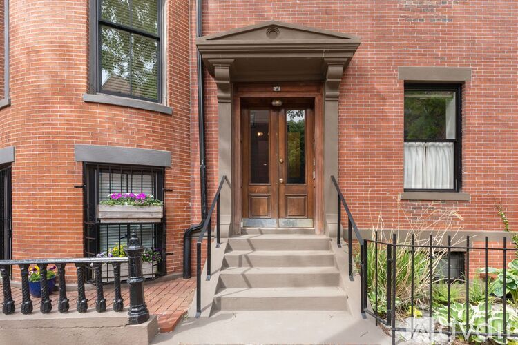 A red brick building with a wooden door and a black railing.