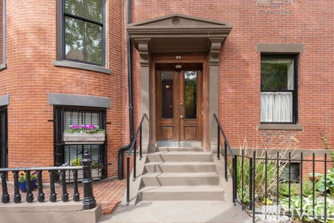 A red brick building with a wooden door and a black railing.