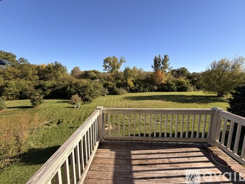 A wooden deck overlooks a grassy field with trees in the distance.