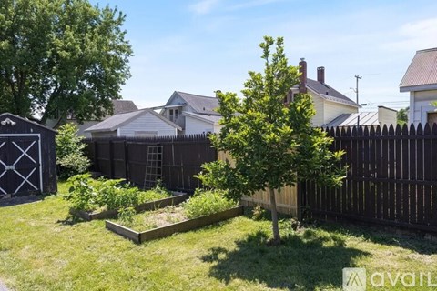 A backyard with a fence, a tree, and a vegetable garden.