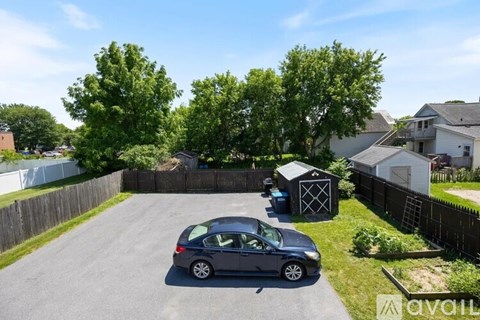 A car is parked in a driveway with a shed and trees in the background.
