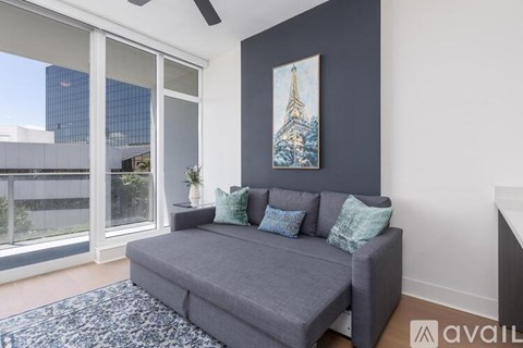 A living room with a grey couch and a painting of a building on the wall.