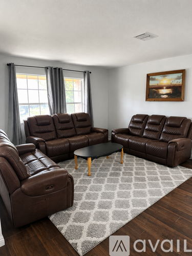 A living room with brown leather furniture and a grey rug.