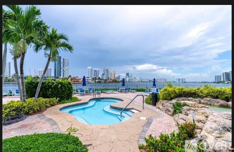 A pool surrounded by greenery and palm trees with a city skyline in the background.