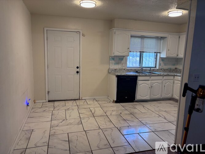A kitchen with white cabinets and a black trash can.