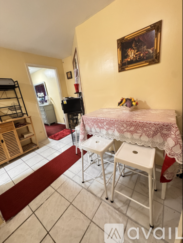 A room with a table and chairs in the foreground and a painting on the wall in the background.