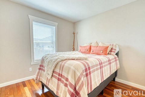 A bedroom with a bed covered in a plaid comforter and a window with blinds.