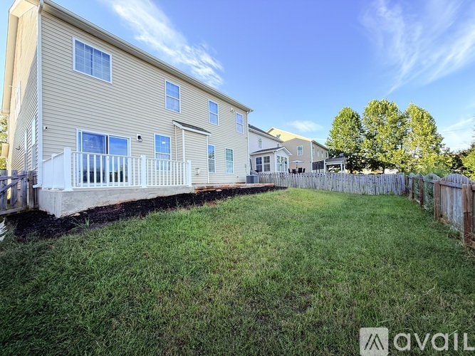 A beige two-story apartment building with a white fence and a green lawn in front.