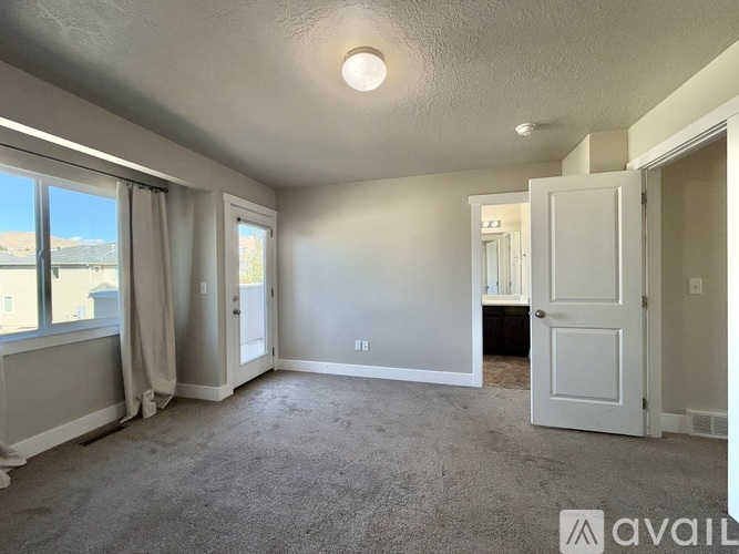 A spacious room with carpeted floor, a window with a view, and a door leading to another room.