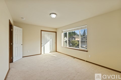A spacious room with a carpeted floor and a large window showing a view of houses and trees outside.