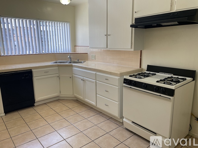 A kitchen with a black dishwasher, white cabinets, and a white stove top oven.