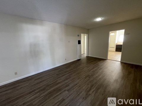 A room with wooden flooring and white walls, with a door on the right side.