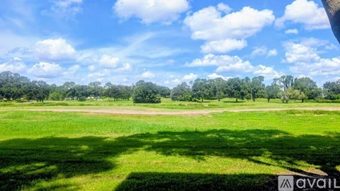 A grassy field with trees in the distance under a blue sky with clouds.