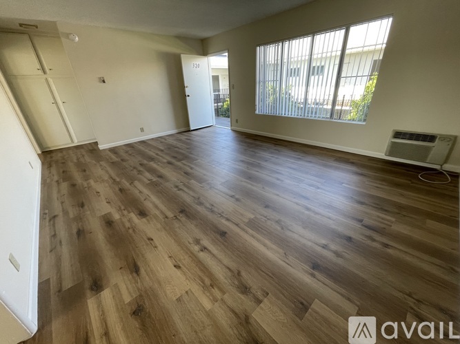A spacious room with wooden flooring and a window with blinds.