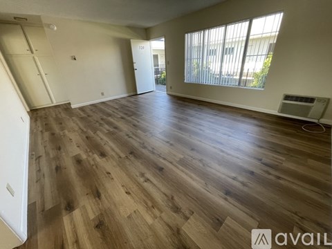 A spacious room with wooden flooring and a window with blinds.