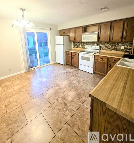 A kitchen with a white stove top oven and microwave, wooden cabinets, and a tiled floor.