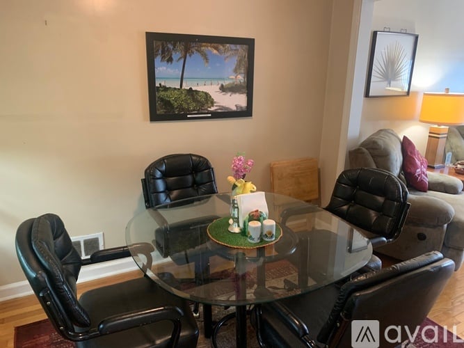 A living room with a glass table and black leather chairs.