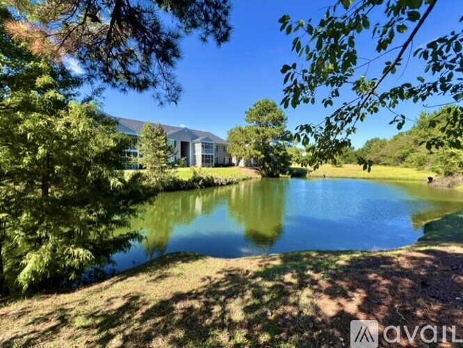 A serene landscape with a pond, trees, and a building in the distance.