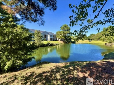 A serene landscape with a pond, trees, and a building in the distance.
