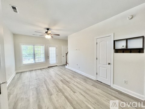 A spacious room with a ceiling fan and light, hardwood flooring, and a large window with blinds.